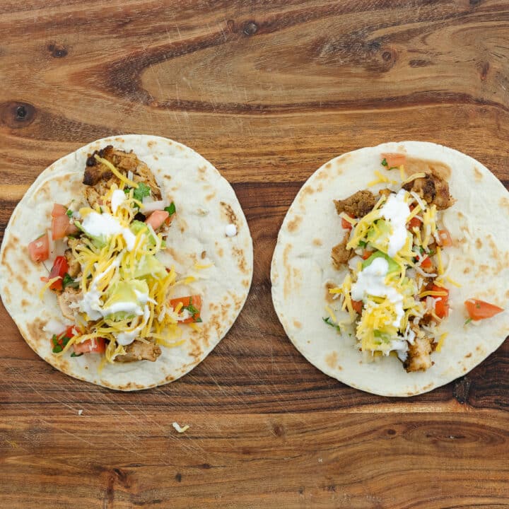 A wooden cutting board with chicken tacos filled with toppings.