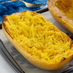 Two halves of baked spaghetti squash on a tray, with a blue towel and a golden fork nearby.
