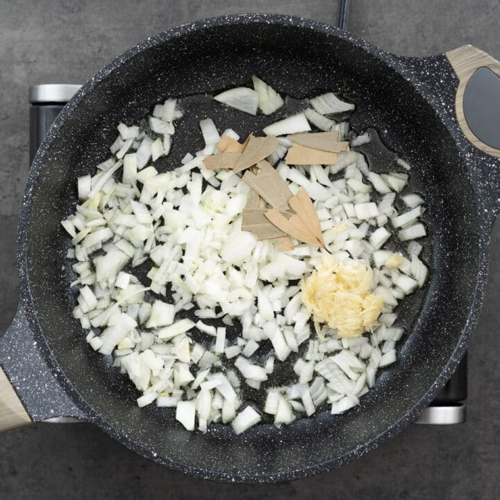 Onions, garlic, and bay leaves in a pan for sauteing.