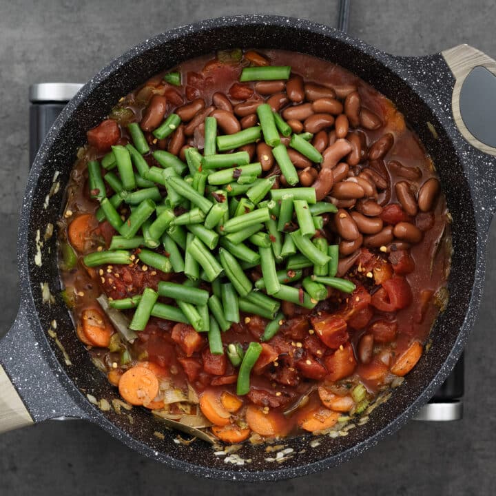 A pan with veggies, beans, and diced tomatoes seasoned with chili flakes.
