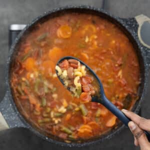 Displaying the hearty veggies and pasta on a blue spoon.