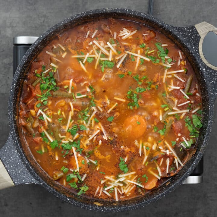 Minestrone Soup garnished with parsley and parmesan cheese in a pan.