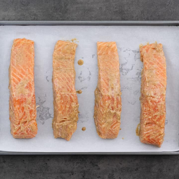 Marinated salmon arranged in a baking tray lined with parchment paper.