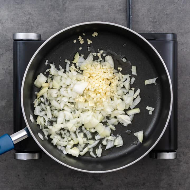 A wide bottom pan with onion and garlic in oil.