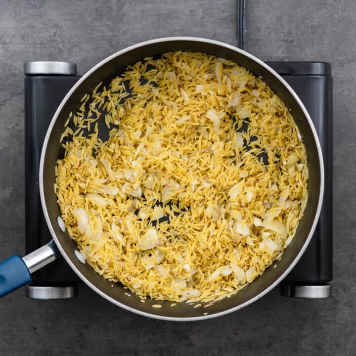 A wide-bottom pan with toasted orzo, onion, and garlic.