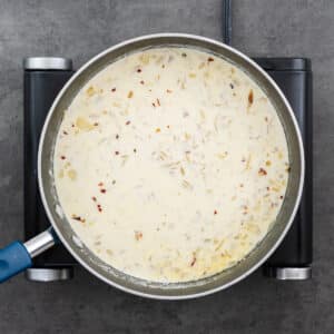 A wide-bottom pan with orzo and half-and-half milk.