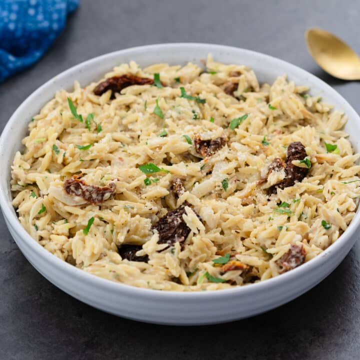 Creamy Orzo served in a white bowl with a golden spoon placed alongside.