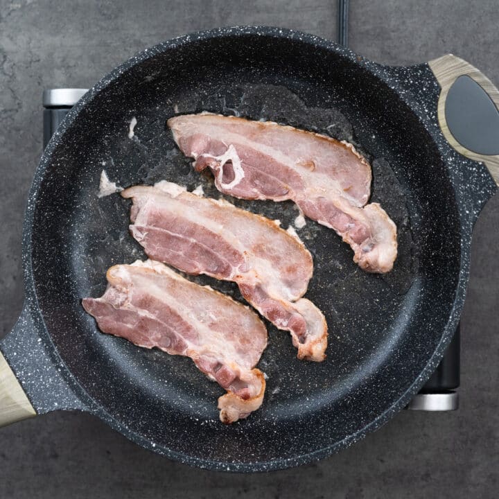 Bacon sizzling in a wide pan on the stove.