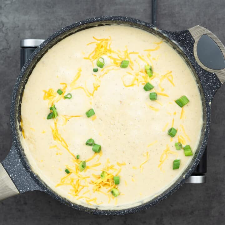 Potato soup garnished with cheddar cheese and green onion in a pan.