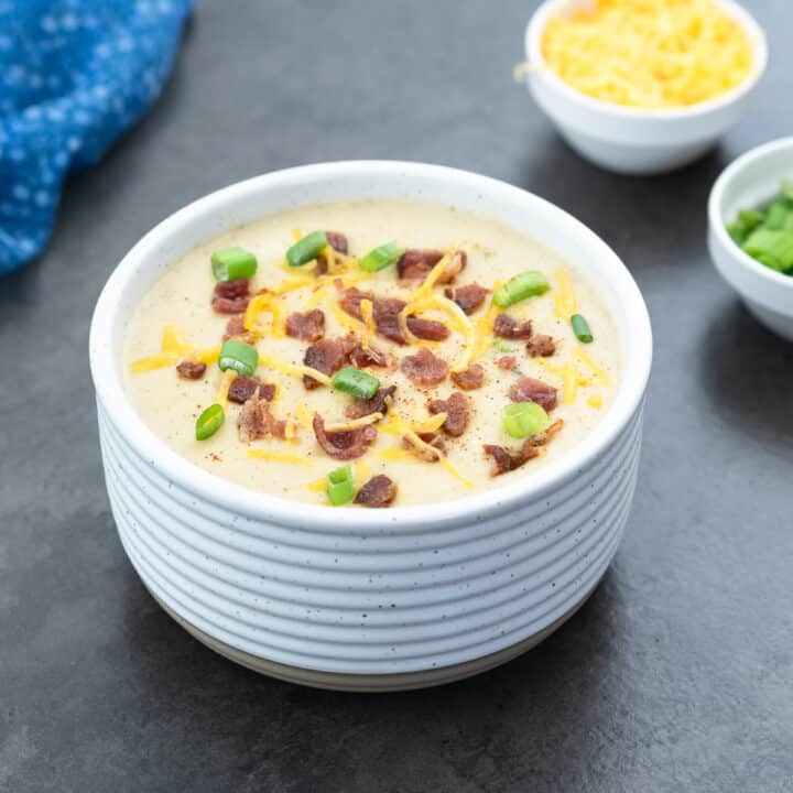 Creamy potato soup served in a white bowl, topped with bacon bits, cheddar cheese, and green onions.