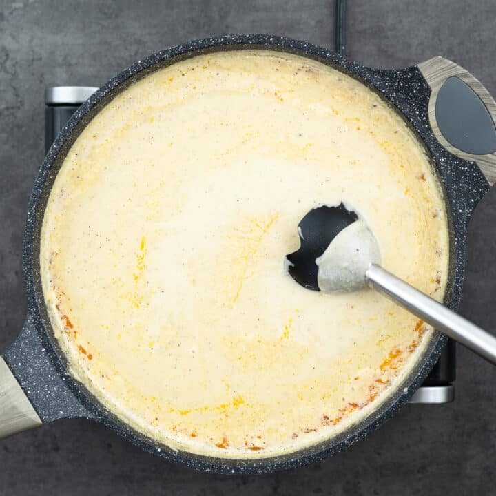 Creamy potato soup being blended with an immersion blender in a pan.