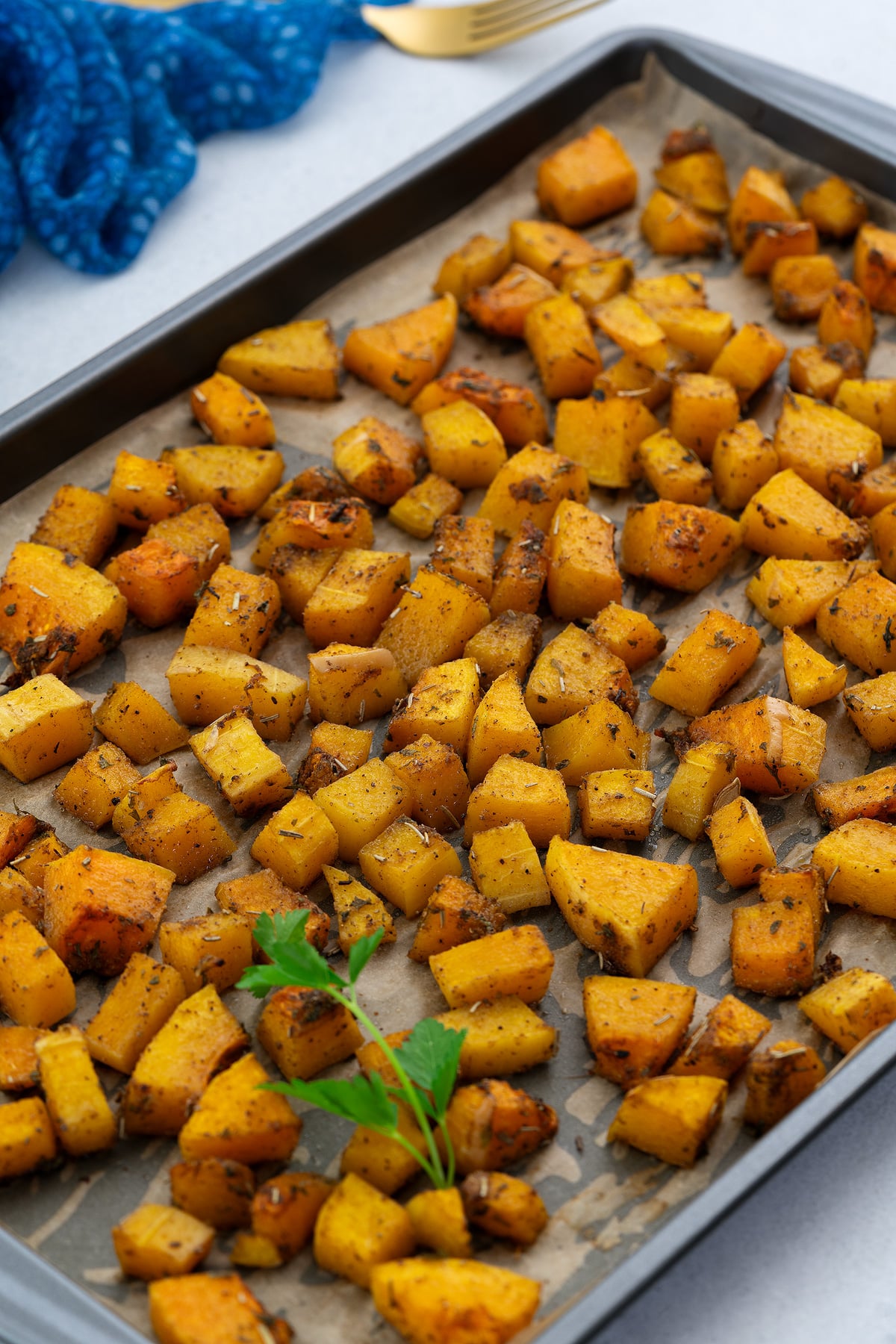 Roasted butternut squash in a baking tray, set on a white table. A fork and a blue towel are neatly placed next to the tray.