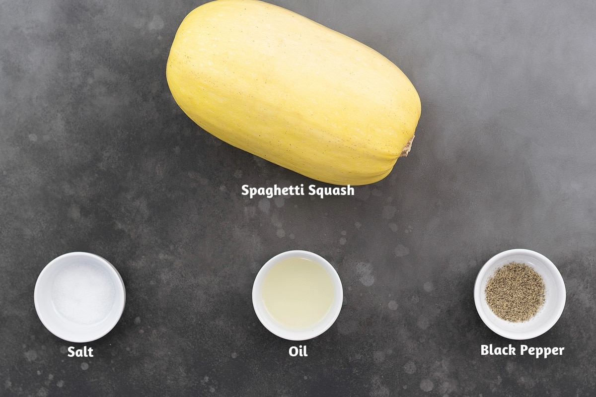 Ingredients for spaghetti squash recipe, including a whole spaghetti squash, salt, oil, and black pepper powder, arranged on a gray table.