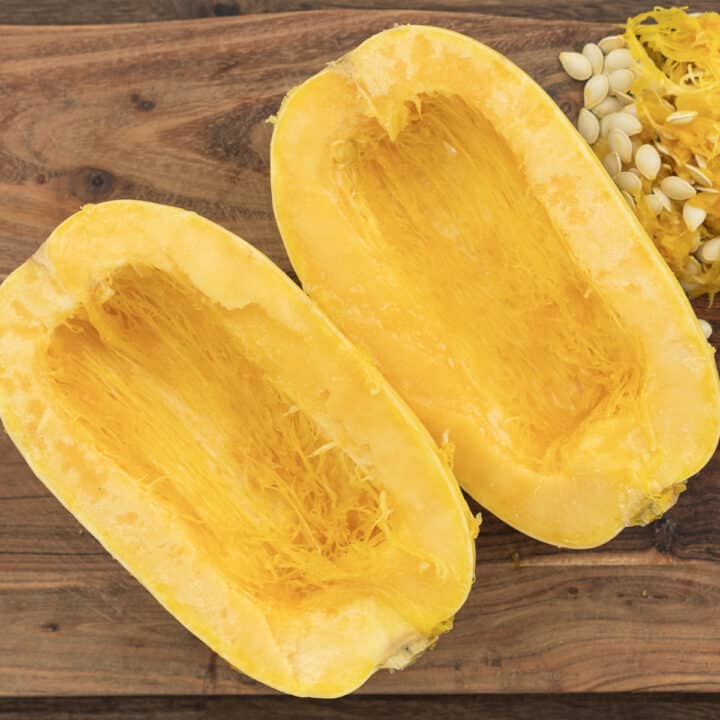 A cutting board with spaghetti squash cut lengthwise into halves with seeds scooped out.
