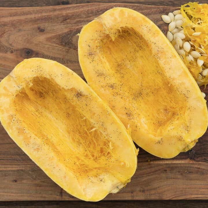 Spaghetti squash seasoned with black pepper and salt placed on a cutting board.