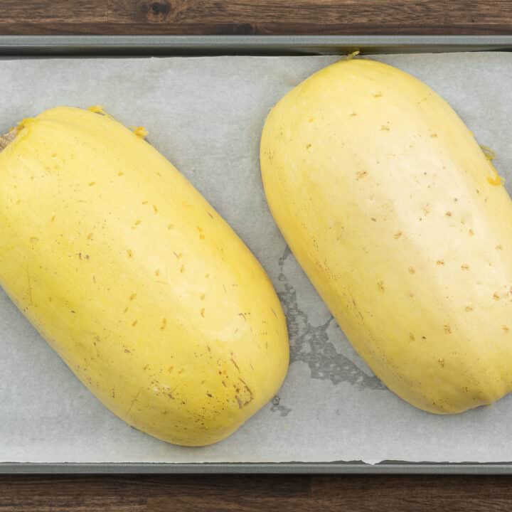 Spaghetti squash placed cut side down on a baking tray lined with parchment paper.