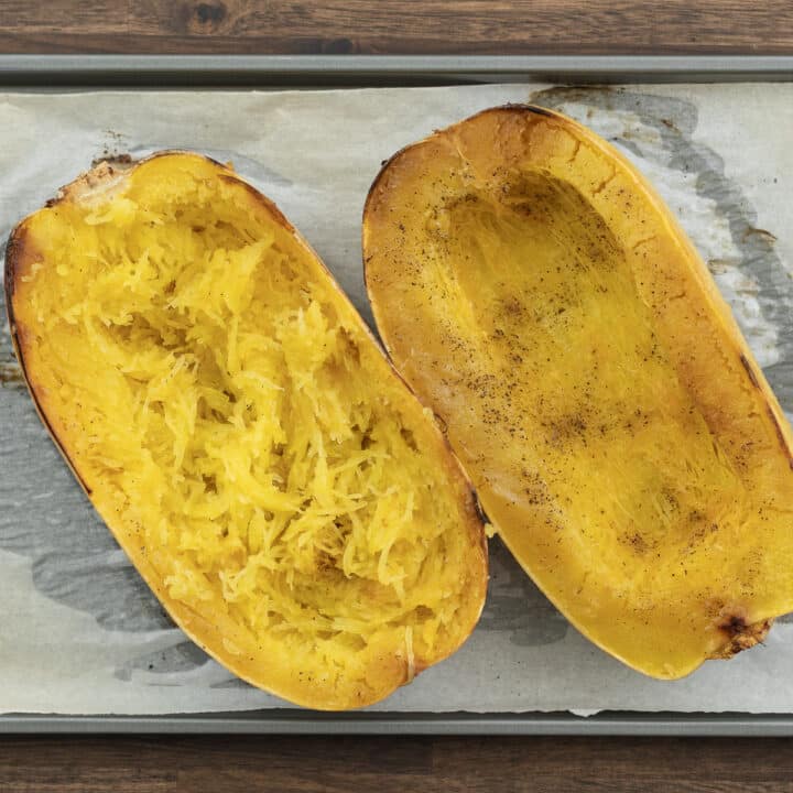 Nicely cooked spaghetti squash on a baking tray with one half scraped.