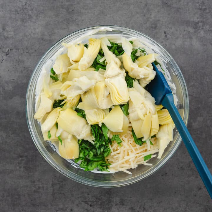 A bowl filled with artichoke and spinach mixed with a creamy base.