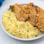 Air fryer chicken tenders on a white plate with couscous on a white table.