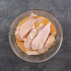 A bowl with chicken tenders in the marinade.