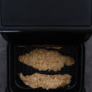 Air fryer basket with crumb-coated chicken tenders.