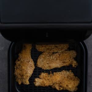 Air fryer basket with half-cooked chicken tenders.