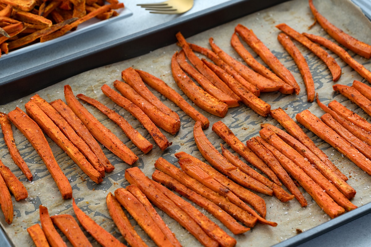 Baked sweet potato fries on a baking tray with a golden fork placed nearby.