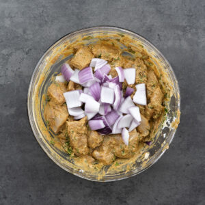 A bowl containing chicken in marinade with onion layers.