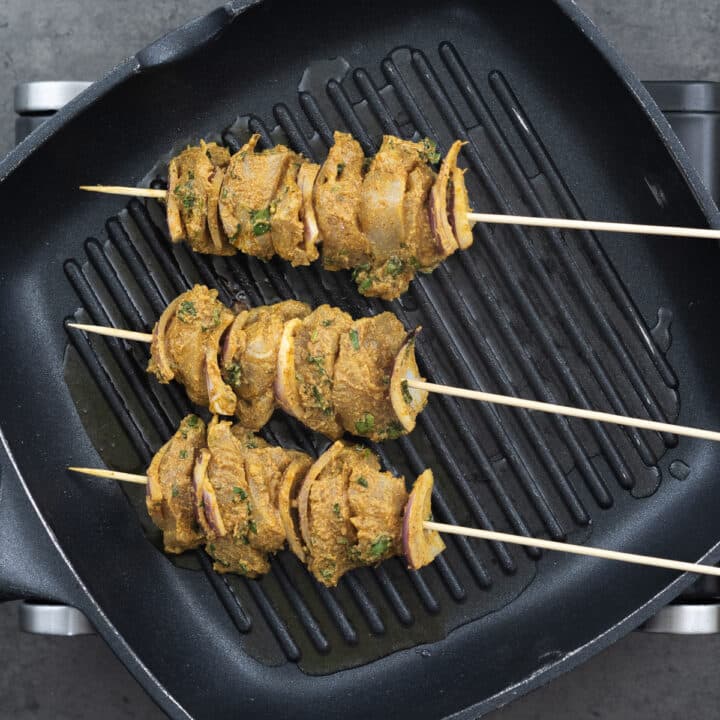 A grilling pan with chicken skewers cooking.