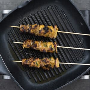A grilling pan with fully grilled chicken kabobs.