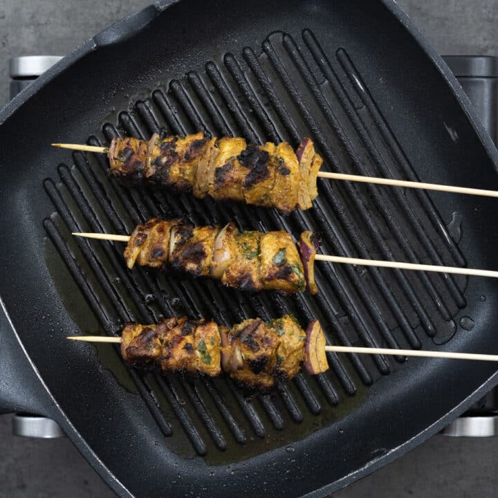 A grilling pan with fully grilled chicken kabobs.