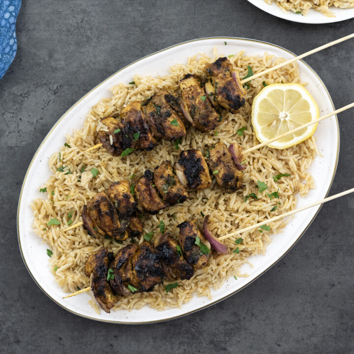 Chicken kabobs served over rice pilaf on an oval plate.