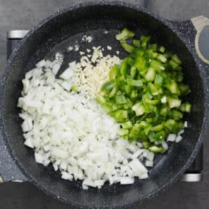 A wide-bottom pot with sautéed onion, garlic, and bell peppers.
