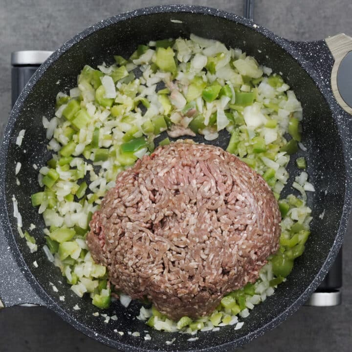 A pot containing ground beef cooked with sautéed aromatics.