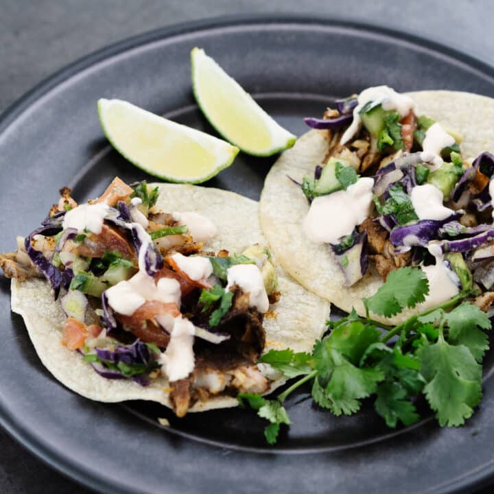 Fish tacos served on a greyish-black plate.