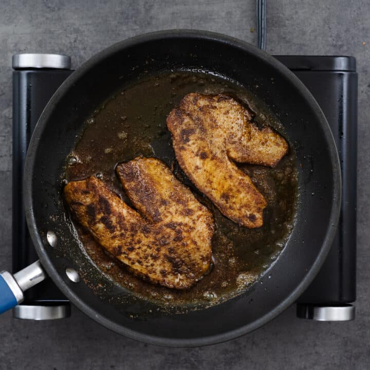 Pan with golden brown tilapia fillets in oil.