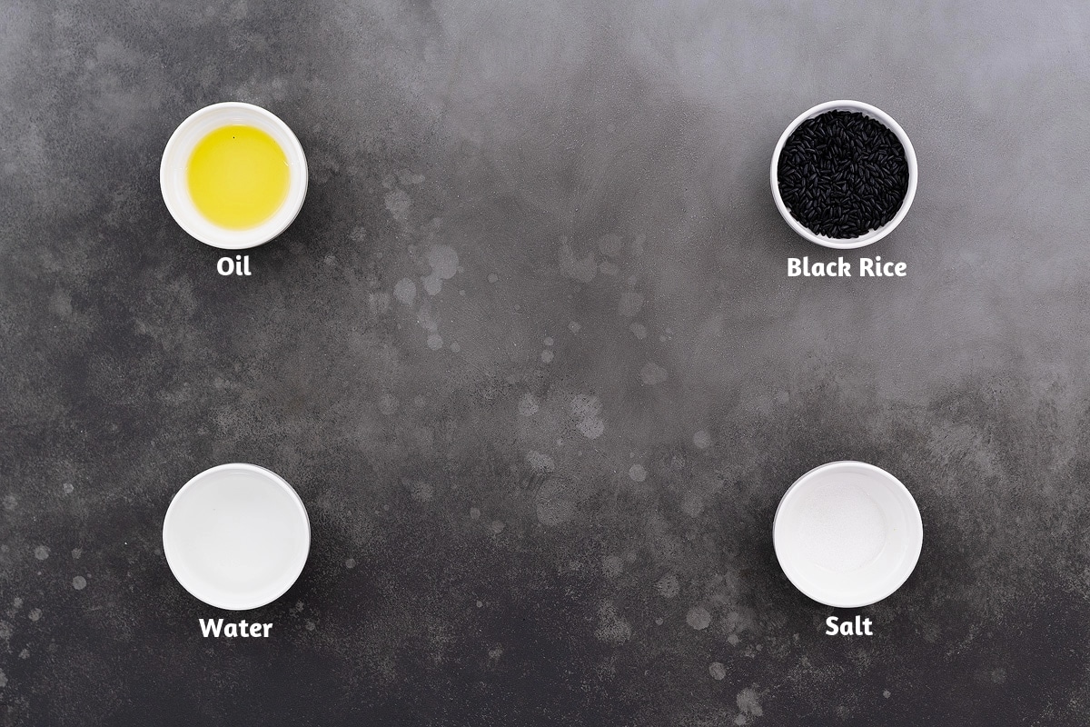Ingredients for forbidden black rice placed on a gray table: oil, black rice, water, and salt.