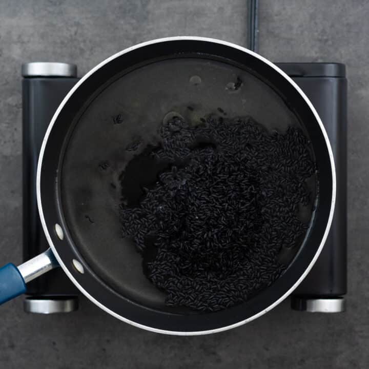 A pot filled with water and black rice, seasoned with salt and oil, ready for cooking.