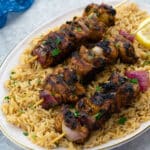 Grilled chicken kabobs on skewers served over a bed of fluffy rice pilaf, set on a white table and a blue towel placed nearby.