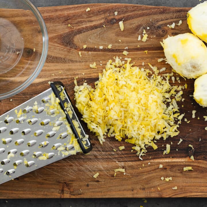 A cutting board with freshly grated lemon zest and a grater.