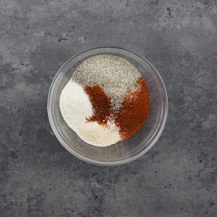 A bowl containing ingredients for homemade seasoned salt, including salt, paprika, garlic powder, onion powder, and black pepper.