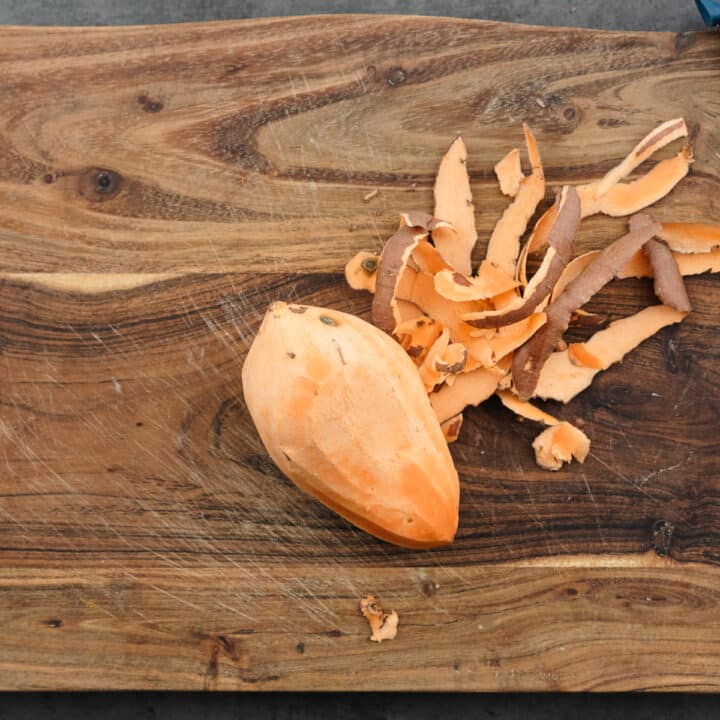 A cutting board with peeled sweet potatoes.
