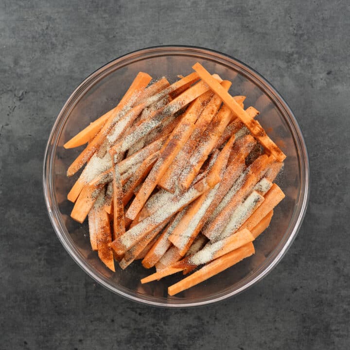 A bowl filled with sliced sweet potatoes sprinkled with seasoning.
