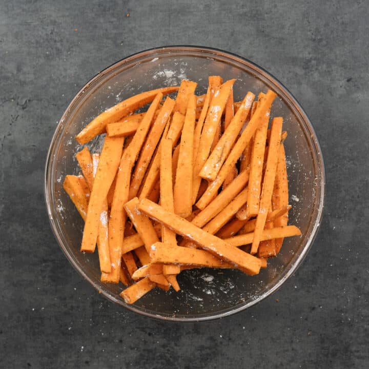 Sweet potatoes coated with cornstarch in a bowl with seasoning.