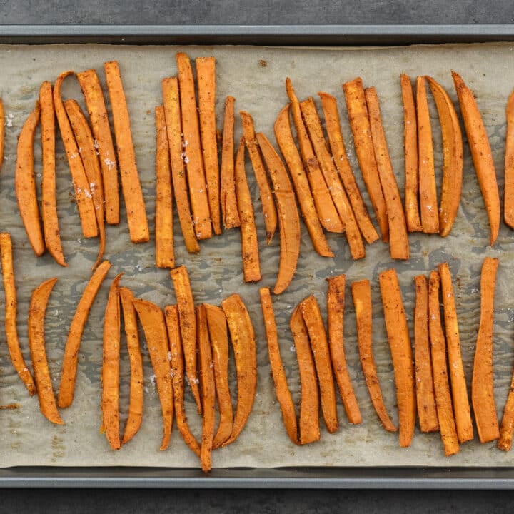 Sweet potato fries in a baking tray seasoned with salt.