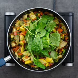 A pot with vegetables and spinach leaves.