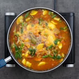 A pot with vegetables and diced tomatoes boiling in a savory vegetable broth.