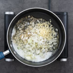 A pan with onion, garlic and bay leaves sizzing in oil butter mixture.