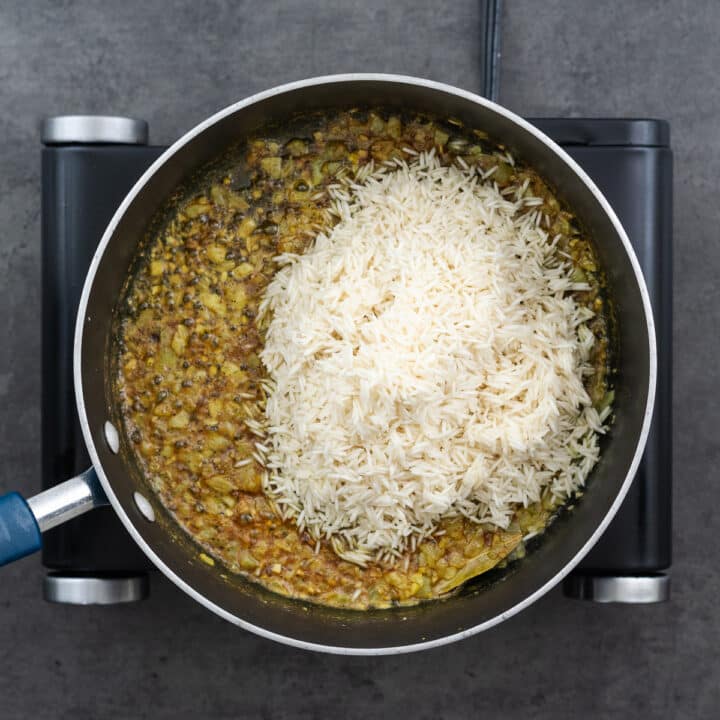 A pan with rice in a oil, butter, spices and onion mixture.