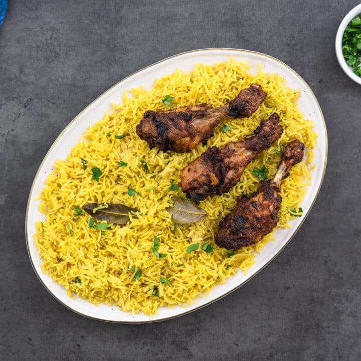 Yellow Rice served in a serving tray with roasted chicken drumsticks.